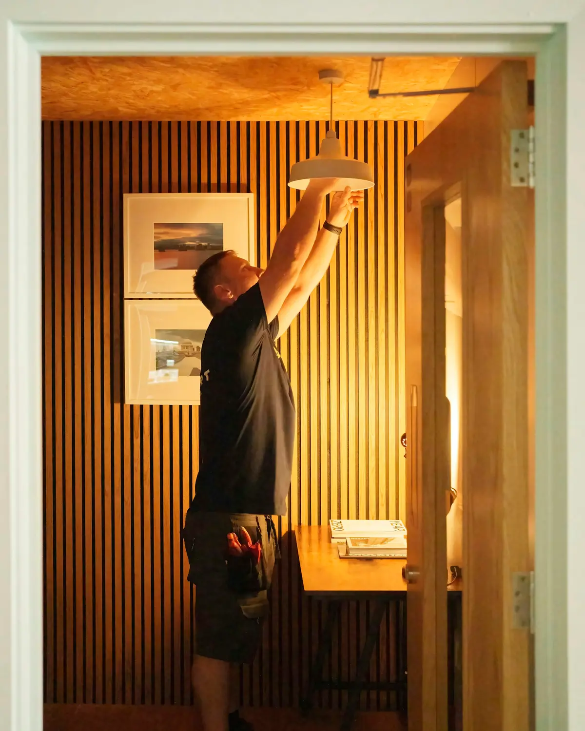 Un électricien installe un luminaire dans un intérieur lambrissé.